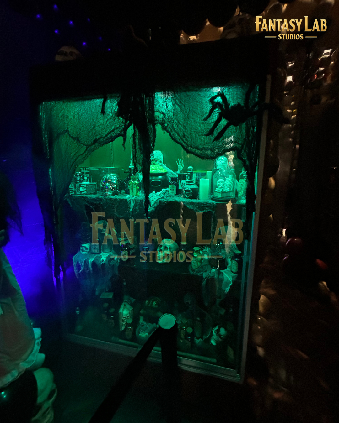 Green-lit apothecary display case packed with jars, props, and cobweb textures.