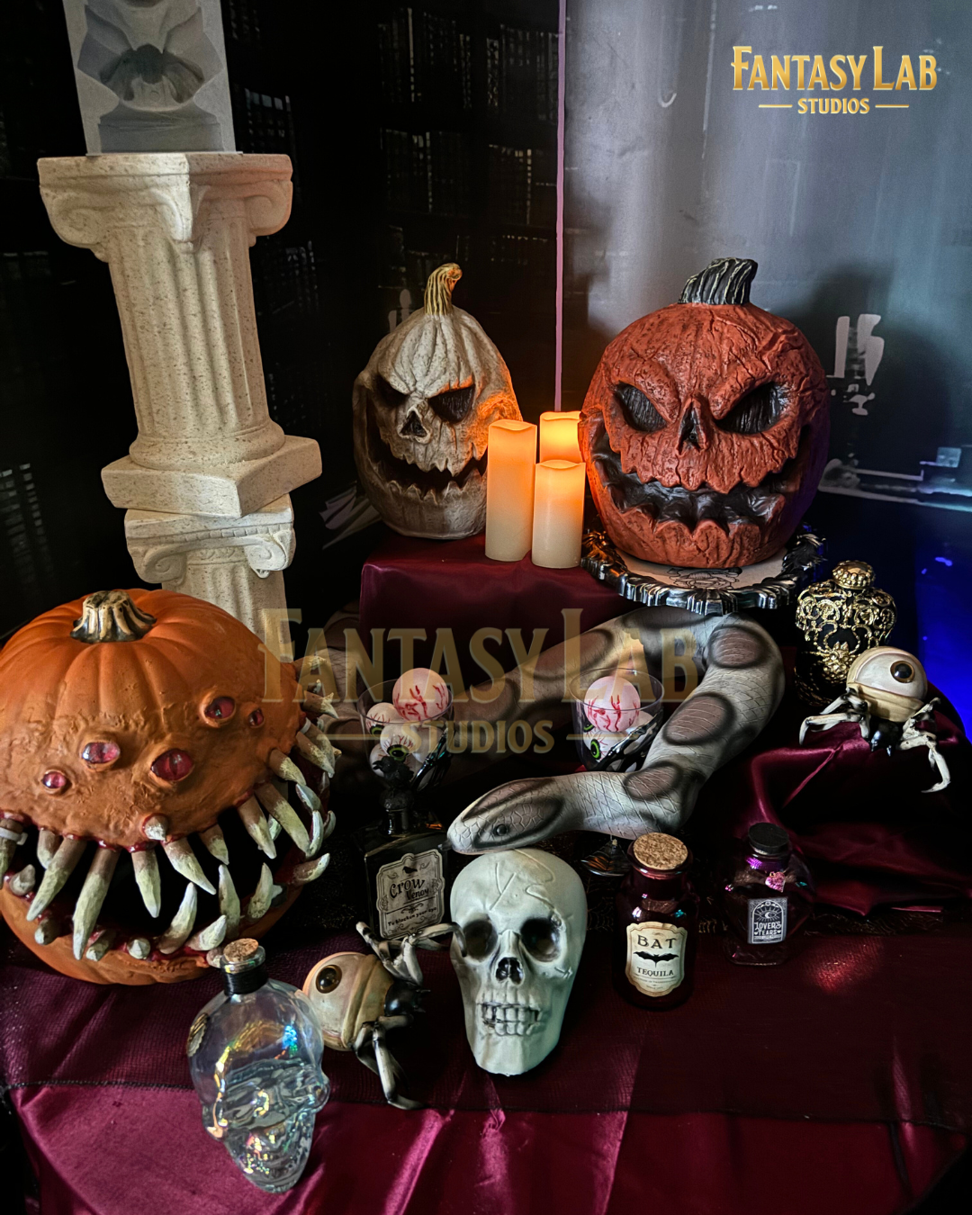 Tabletop of sculpted Halloween props: carved pumpkins, skulls, eyeball jars, and candles.