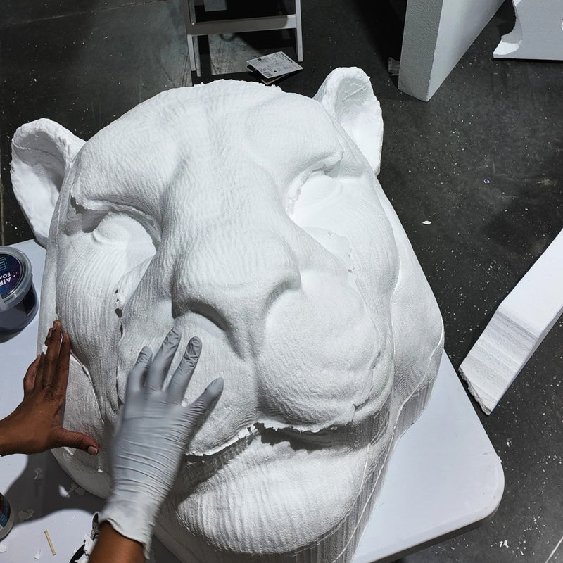 White sculpture of a bear panther being worked on with hands wearing gloves.