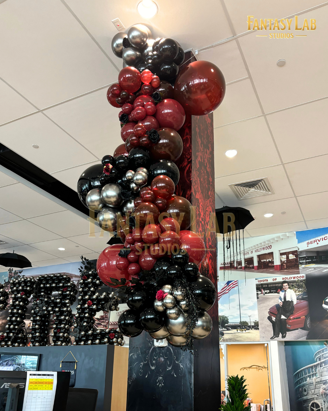 Metallic red and black balloon column with rose accents on a showroom pillar.